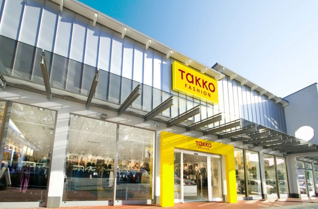 Eingangsbereich eines Takko Stores von außen mit großen Takko Fashion Logo über dem Eingang